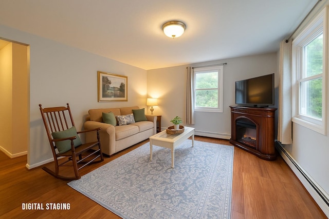 living area featuring a baseboard radiator, wood finished floors, and a glass covered fireplace