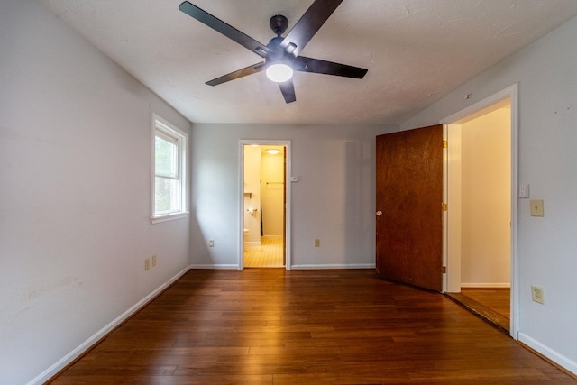 unfurnished bedroom featuring hardwood / wood-style flooring, baseboards, ensuite bath, and a ceiling fan