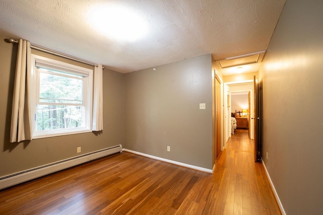 spare room featuring a baseboard radiator, wood finished floors, attic access, baseboards, and a textured ceiling