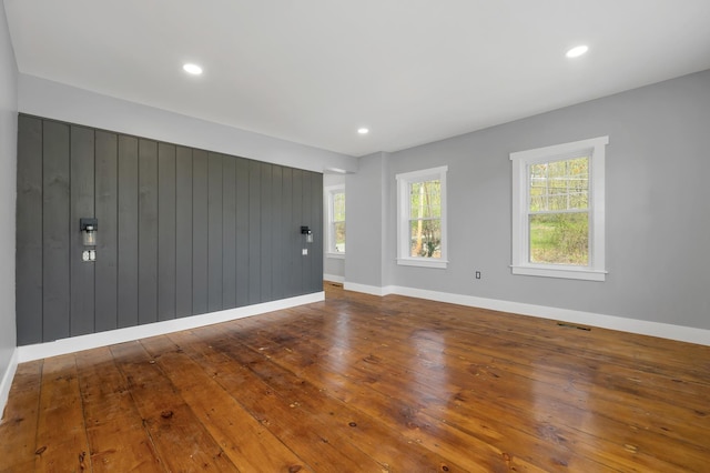 unfurnished living room with hardwood / wood-style floors, baseboards, wooden walls, and recessed lighting
