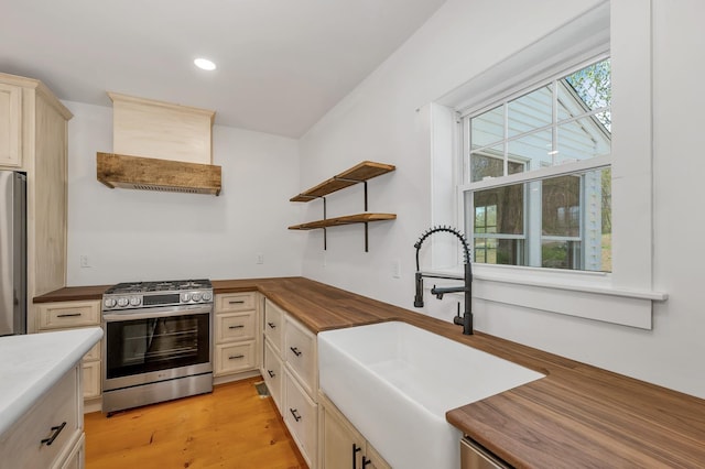 kitchen with appliances with stainless steel finishes, a sink, wooden counters, premium range hood, and recessed lighting