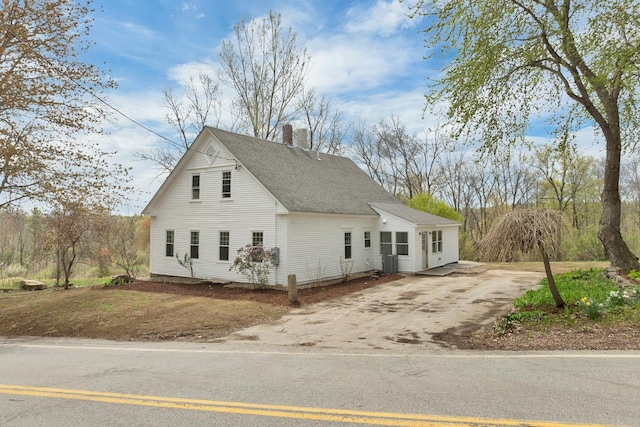 view of side of property featuring driveway, a chimney, and roof with shingles