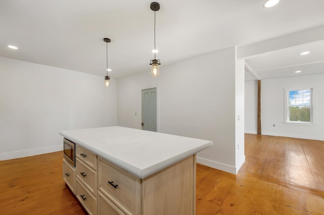 kitchen featuring stainless steel microwave, a kitchen island, light wood-type flooring, light countertops, and recessed lighting
