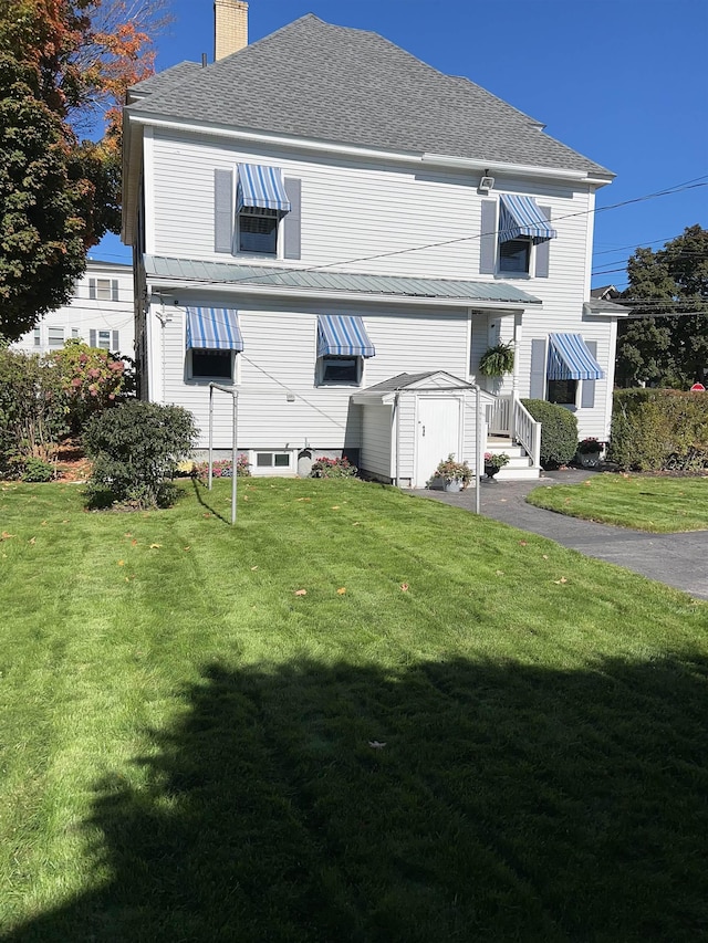 rear view of property featuring a chimney, a storage unit, a lawn, and an outbuilding