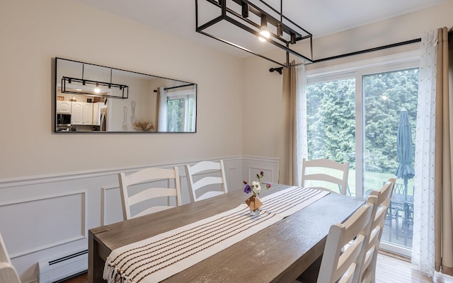dining room with a baseboard heating unit, healthy amount of natural light, a decorative wall, wainscoting, and a chandelier