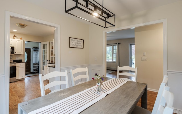 dining room with light wood-style floors, a baseboard radiator, wainscoting, and a chandelier