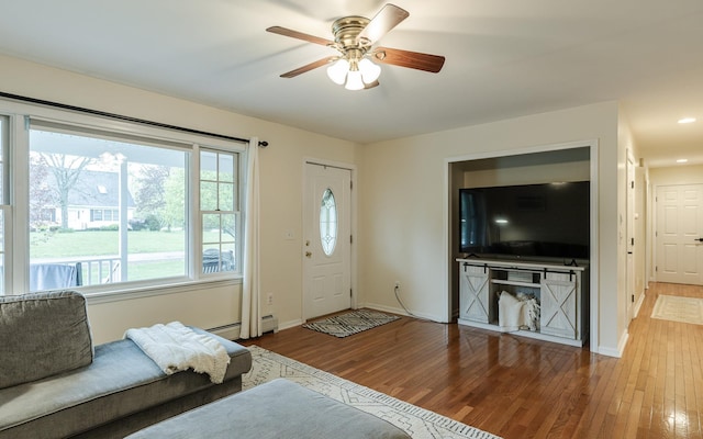 living area featuring wood finished floors, a ceiling fan, baseboards, and a baseboard radiator