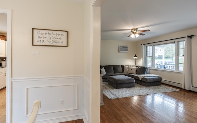 living room with a ceiling fan, wood finished floors, wainscoting, baseboard heating, and arched walkways