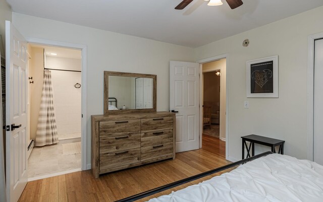 bedroom featuring light wood-style flooring, baseboards, ensuite bathroom, ceiling fan, and a baseboard heating unit