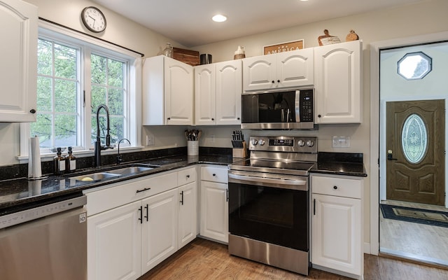 kitchen with stainless steel appliances, a sink, white cabinetry, light wood-type flooring, and dark stone countertops
