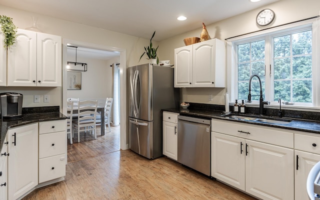 kitchen featuring appliances with stainless steel finishes, a sink, light wood-style flooring, white cabinetry, and dark stone countertops