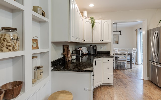 kitchen with freestanding refrigerator, light wood-style floors, white cabinets, built in study area, and dark stone counters