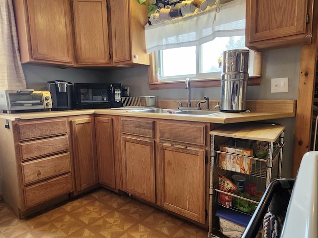 kitchen featuring black microwave, a sink, light countertops, and brown cabinetry