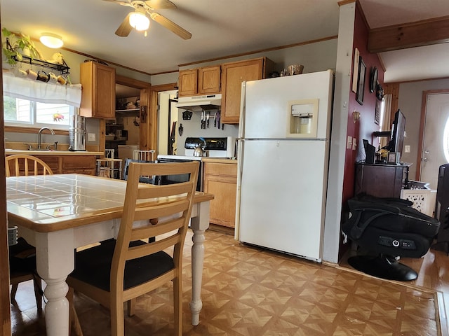 kitchen featuring white appliances, tile counters, under cabinet range hood, a ceiling fan, and a sink