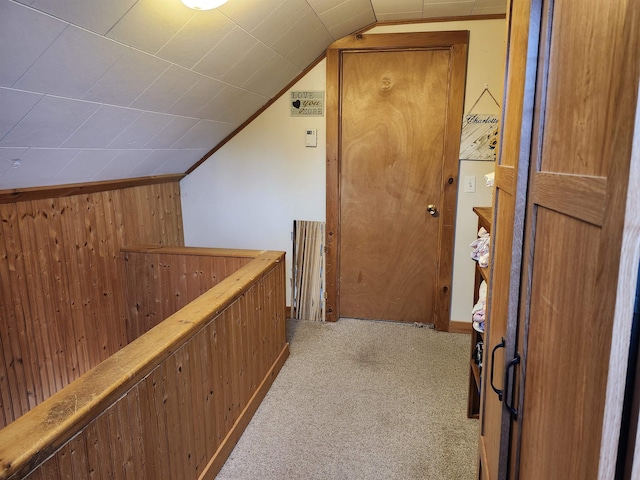 hall with lofted ceiling, carpet, wooden walls, and an upstairs landing