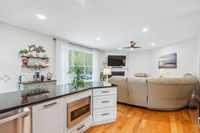 11 Carriage Hill Rd, Wilton, NH 03086 - kitchen with stainless steel appliances, dark countertops, a fireplace, white cabinetry, and a ceiling fan