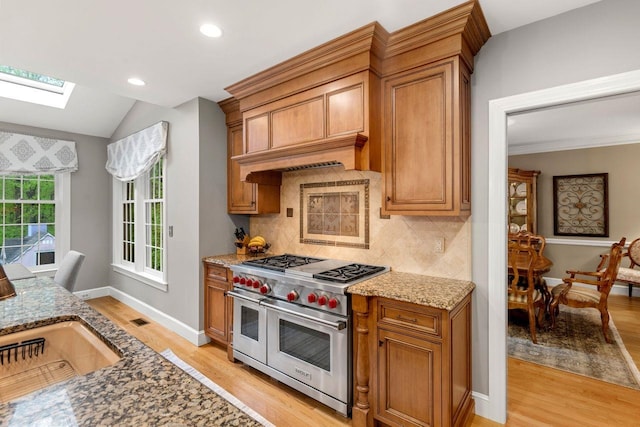 12 Mcintosh Ln, Bedford, NH 03110 - kitchen with range with two ovens, a skylight, light wood finished floors, light stone countertops, and brown cabinets