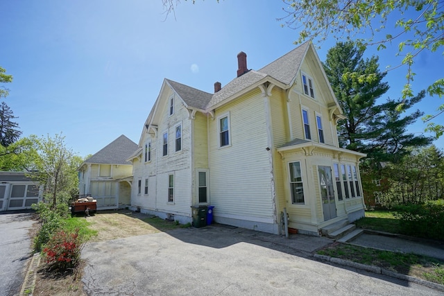 489 Hanover St, Manchester, NH 03104 - view of side of home with a chimney, entry steps, an outbuilding, roof with shingles, and a storage unit