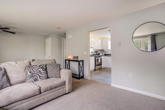 living area with light colored carpet, a ceiling fan, and baseboards