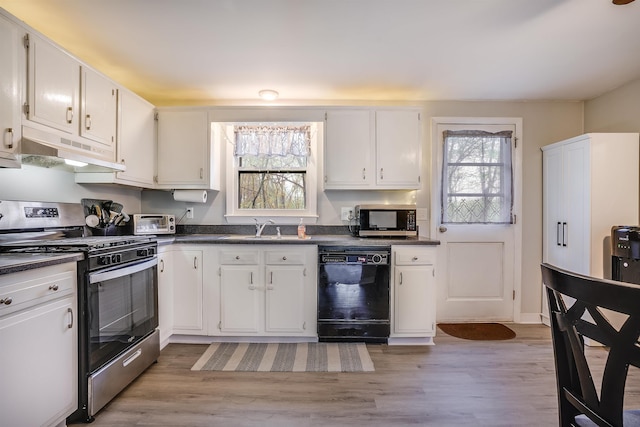 kitchen featuring stainless steel appliances, under cabinet range hood, dark countertops, a sink, and white cabinets