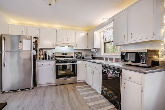 kitchen featuring stainless steel appliances, a sink, under cabinet range hood, dark countertops, and white cabinets