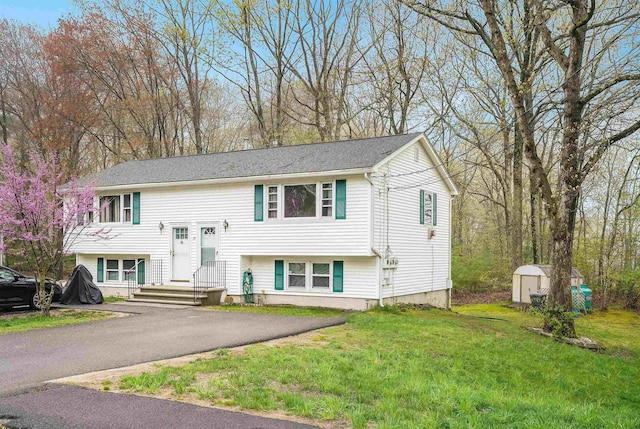 raised ranch featuring a shed, an outdoor structure, a front lawn, and asphalt driveway