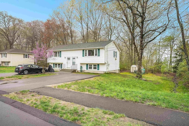 bi-level home with asphalt driveway, a front yard, a storage shed, and an outbuilding