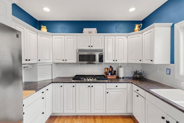 38 Farmington Rd, Nashua, NH 03060 - kitchen featuring appliances with stainless steel finishes, white cabinetry, decorative backsplash, light wood-style flooring, and a sink