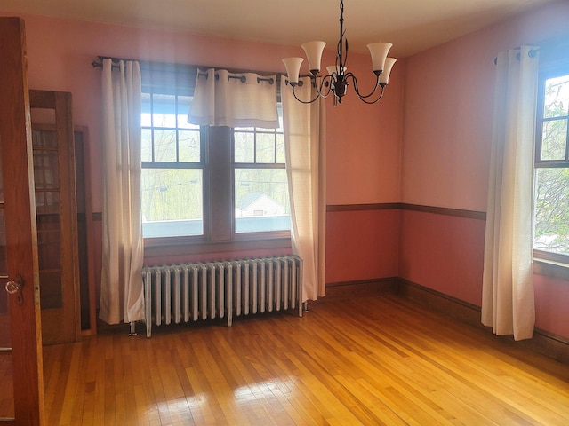 unfurnished room with radiator, light wood finished floors, and a chandelier