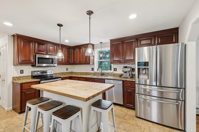 kitchen with stainless steel appliances, a sink, wood counters, backsplash, and a kitchen breakfast bar