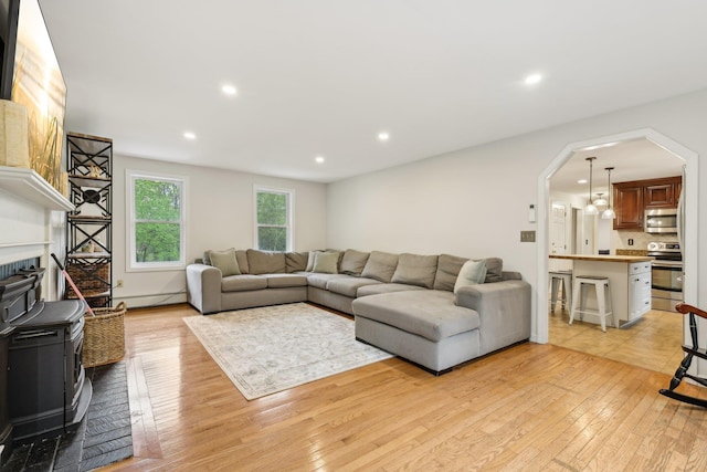 living room with light wood-type flooring, arched walkways, recessed lighting, a wood stove, and a baseboard heating unit