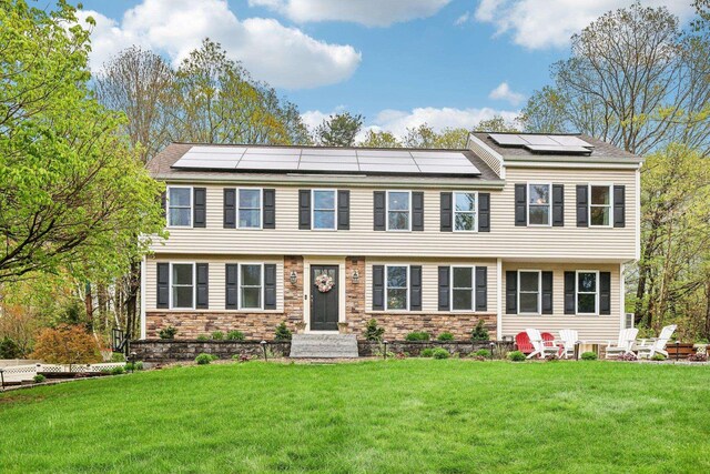 view of front of house with a front yard, solar panels, and stone siding