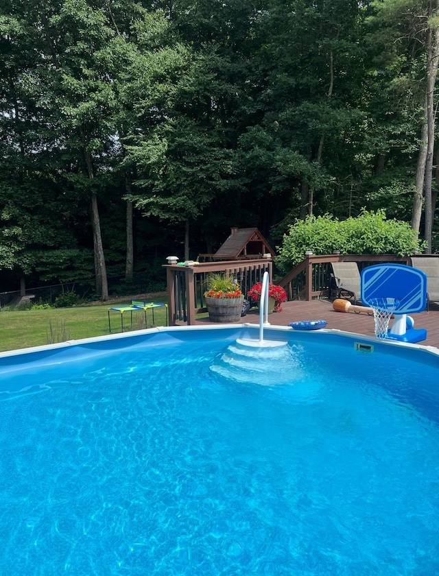 outdoor pool with a wooden deck and a view of trees