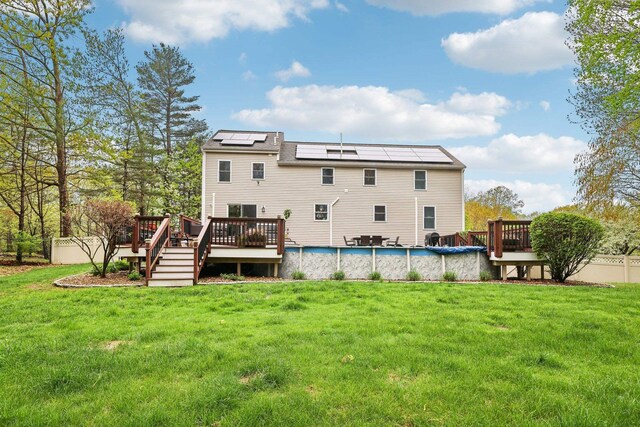rear view of property with a deck, roof mounted solar panels, and a covered pool