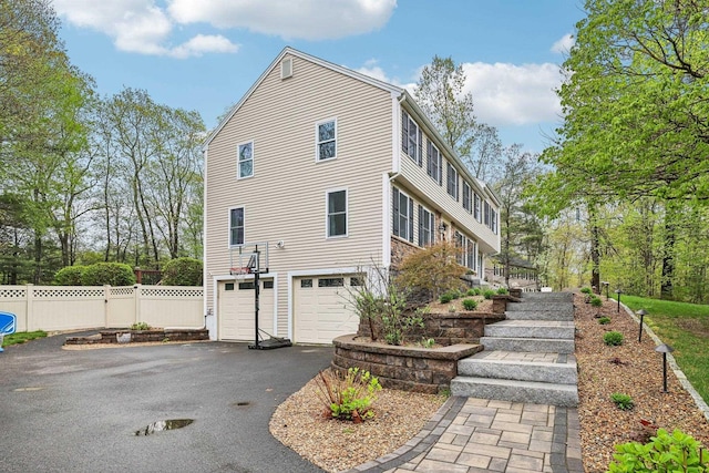 view of property exterior with a garage, asphalt driveway, and fence