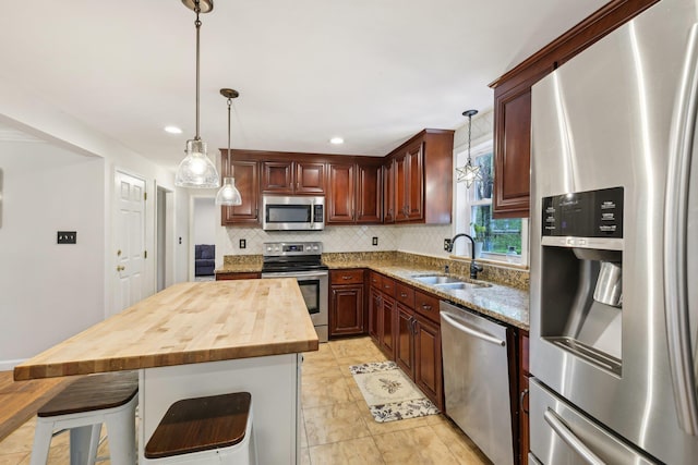 kitchen with appliances with stainless steel finishes, a sink, decorative backsplash, butcher block counters, and a breakfast bar area