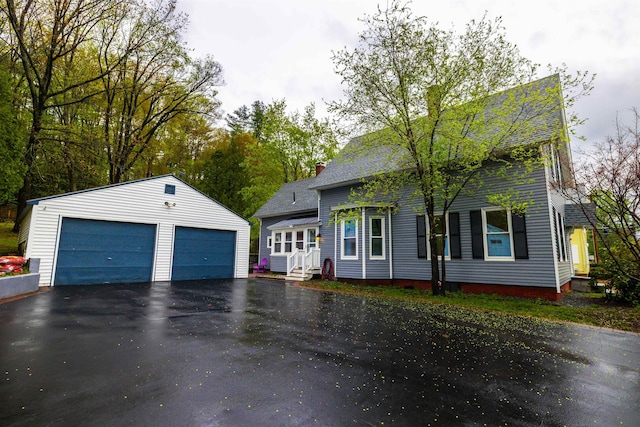 view of front of home featuring an outdoor structure, a detached garage, a chimney, and roof with shingles