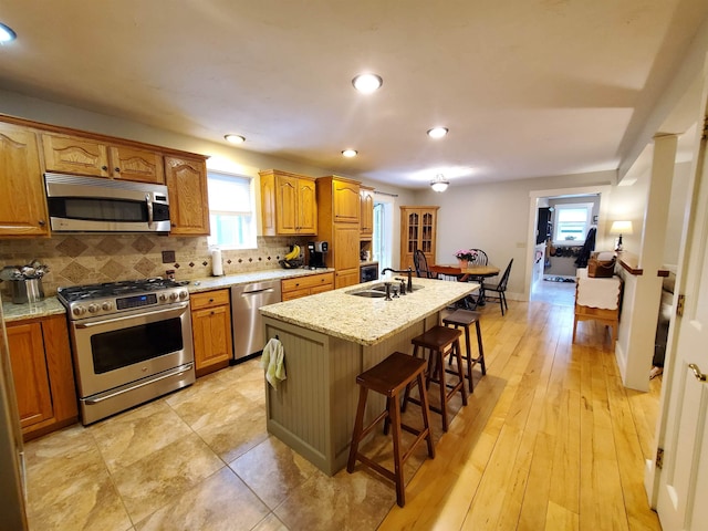 kitchen featuring appliances with stainless steel finishes, a kitchen breakfast bar, backsplash, a center island with sink, and light stone countertops