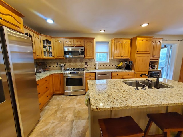 kitchen featuring stainless steel appliances, a sink, light stone countertops, a kitchen bar, and recessed lighting