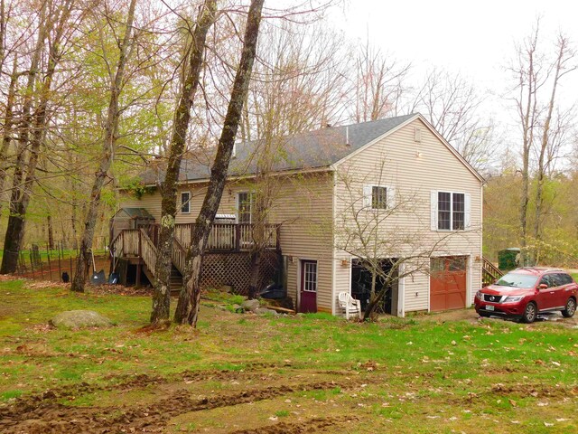 back of house featuring stairway, an attached garage, a deck, and a yard