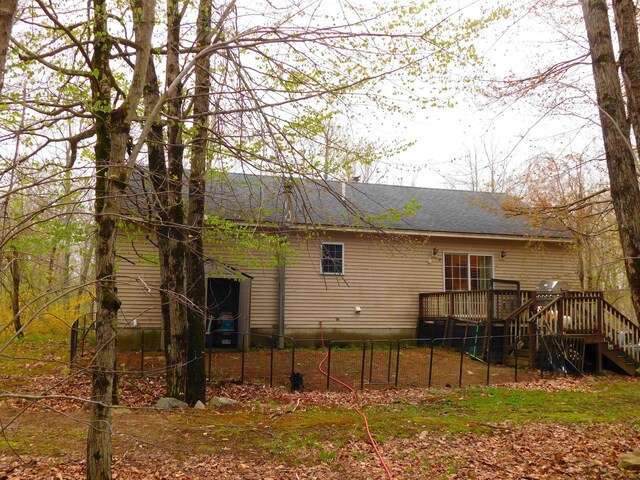 rear view of house with a deck, stairs, fence, and roof with shingles