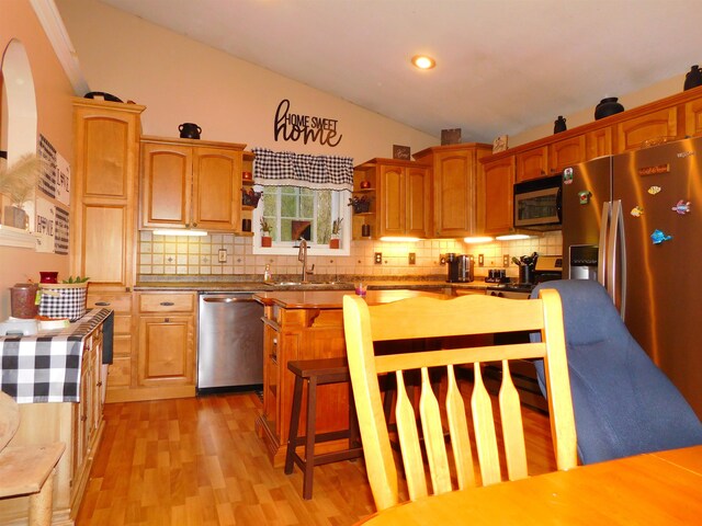 kitchen featuring stainless steel appliances, a sink, backsplash, light wood-type flooring, and vaulted ceiling