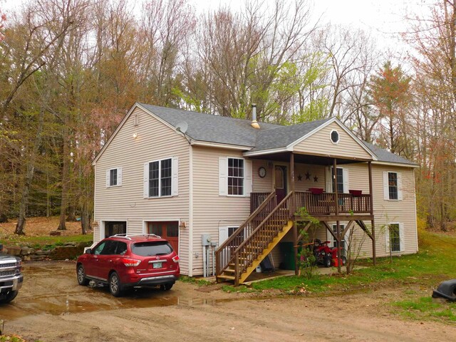 view of front of home with an attached garage, stairway, dirt driveway, and roof with shingles