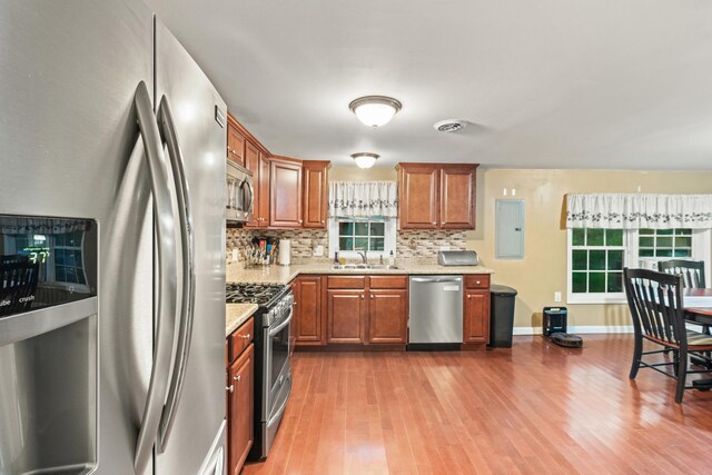 kitchen featuring appliances with stainless steel finishes, a sink, backsplash, wood finished floors, and light stone countertops