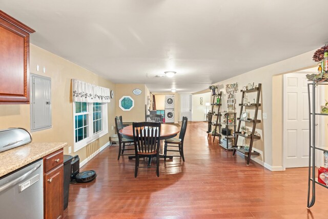 dining area featuring stacked washer and clothes dryer, electric panel, wood finished floors, and baseboards