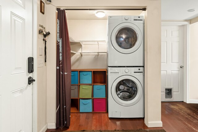clothes washing area featuring stacked washer and clothes dryer, wood finished floors, and baseboards