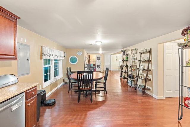 dining area featuring electric panel, stacked washer / dryer, wood finished floors, and baseboards