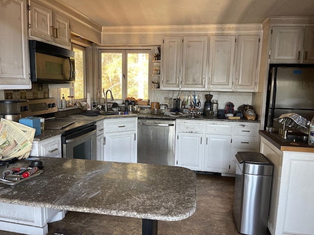 kitchen with stainless steel appliances, a sink, dark stone countertops, white cabinets, and ornamental molding