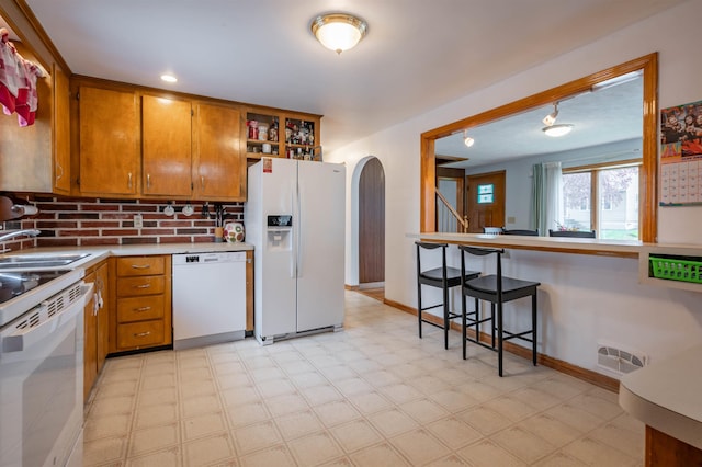 kitchen featuring white appliances, arched walkways, brown cabinetry, light flooring, and a sink