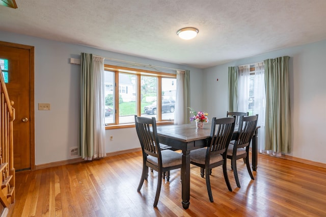 dining space with light wood finished floors, plenty of natural light, a textured ceiling, baseboards, and stairway
